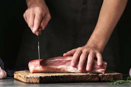 A butcher slicing a fresh cut of meat on a wooden board