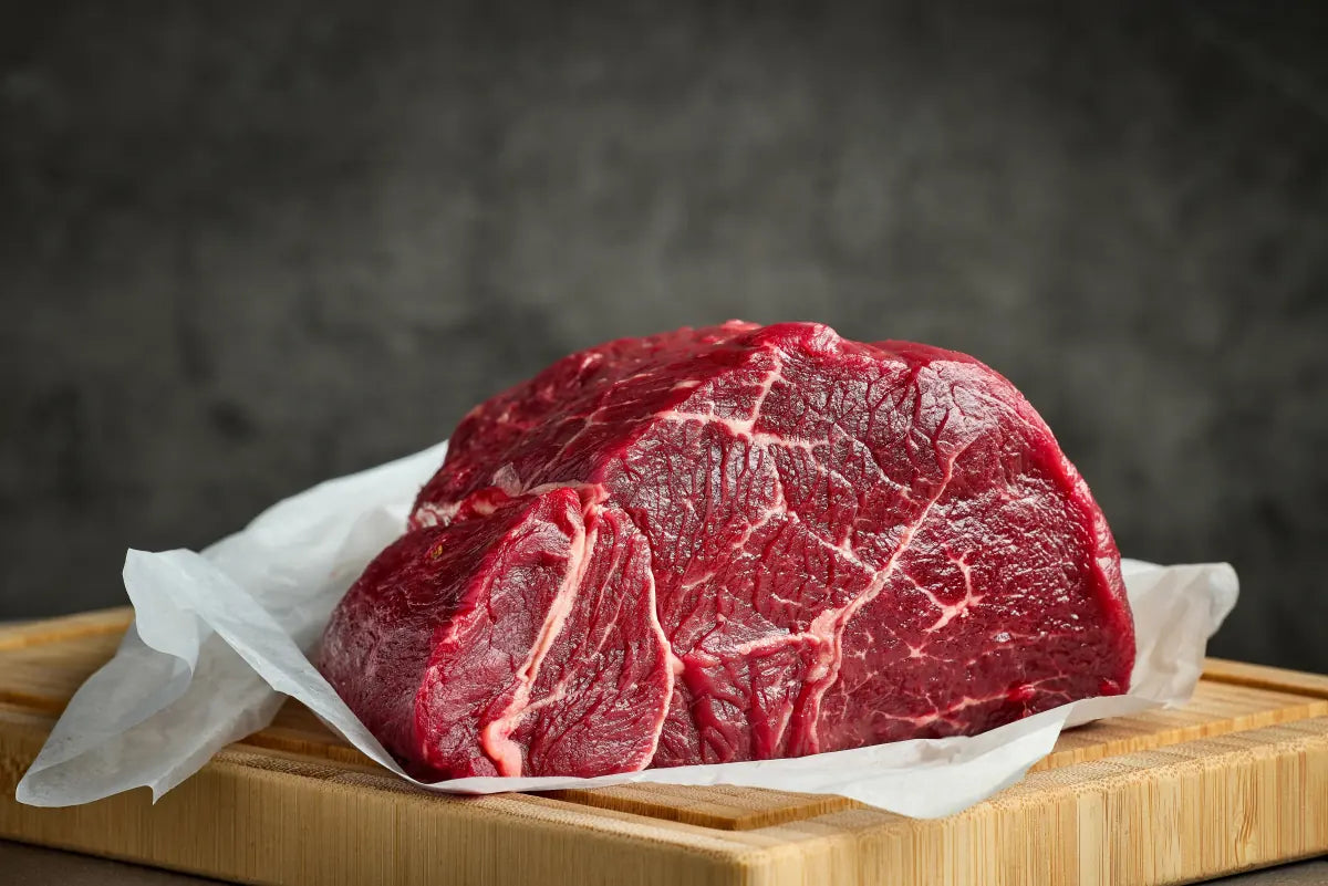 A fresh cut of beef on butcher's paper on a wooden board